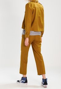 Senapsgul kort jacka med knap stängning och matchande byxor. Bärs med marinblå sneakers och blå randiga strumpor. Slät textur.