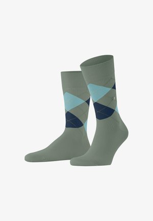 Un paio di calzini verde oliva a metà polpaccio con un motivo a rombi argyle blu e blu navy sui lati, su uno sfondo bianco.