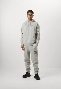 Grå huvtröja och matchande mjukisbyxor av mjukt tyg. Huvan har dragsko, kanguruficka och tryckt logotypdetalj på byxorna.