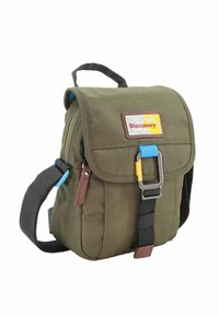 Mochila de tela verde con cierre de solapa, correa negra ajustable, acentos azules y un parche de logo amarillo y rojo en la parte frontal.