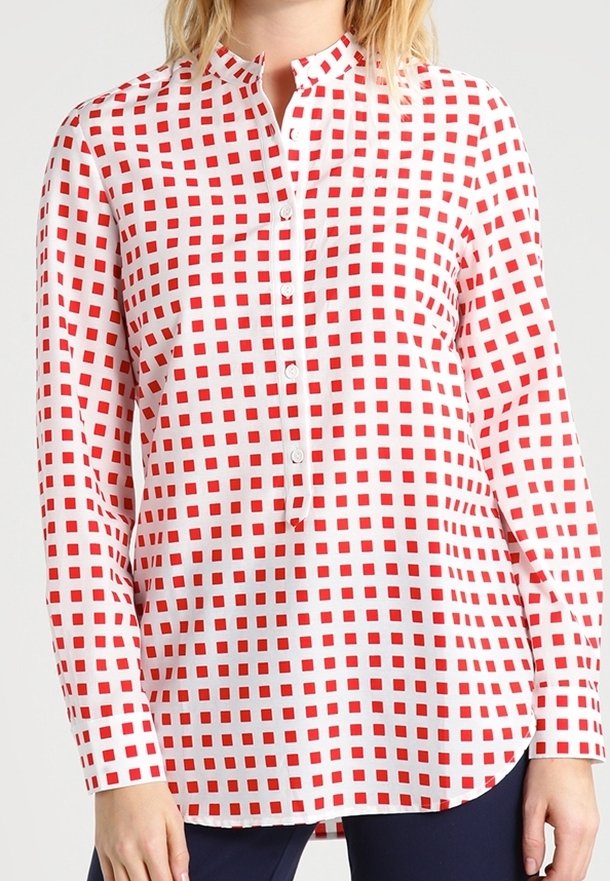 Nainen, jolla on päällään pitkähihainen valkoinen paita, jossa on punainen ruutukuviokokoelma ja osittainen nappitasku, yhdistettynä tummiin housuihin.