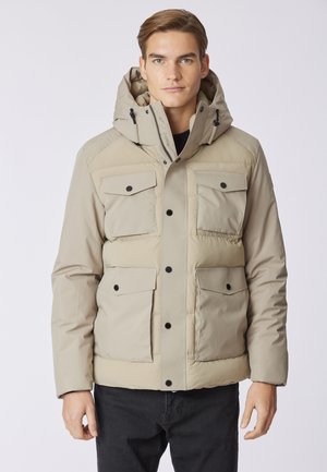 Giacca a vento beige con cappuccio, dotata di quattro tasche frontali, bottoni neri e una texture liscia, progettata per il calore e la funzionalità.