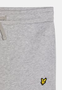 Pantalon de survêtement gris avec une texture douce, une taille élastique et un petit logo d'oiseau jaune brodé sur la jambe inférieure gauche.