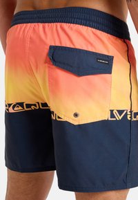 Herrbadshorts med en gradientdesign som går från orange till marinblå. Har en bakficka och resårmidja. Tyget verkar vara lätt.