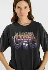 Camiseta negra de gran tamaño con un estampado gráfico colorido que presenta texto de estilo retro y cerezas. Tela de algodón con una textura suave.