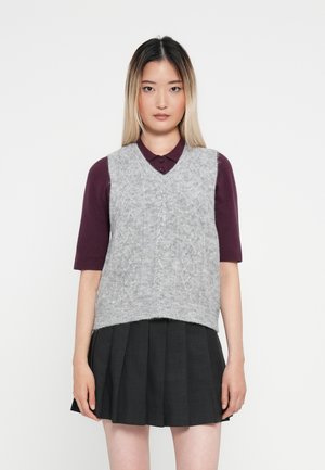 Grå strikket vest med kabelmønster over en burgunder skjorte med krage, kombinert med et svart plissé skjørt. Enkel design, myk tekstur og uformell stil.