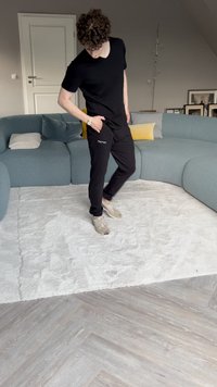 Black t-shirt and black pants worn by a person on a plush white rug, with a curved blue couch and decorative pillows in the background.