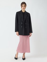Blazer noir à double boutonnage avec revers cranté, porté sur une robe midi en satin rose, complété par des escarpins noirs à bout pointu.
