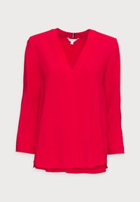 Blusa a maniche lunghe con scollo a V di un rosso vivo, caratterizzata da una texture liscia e aperture laterali per facilitare il movimento. Tessuto leggero.