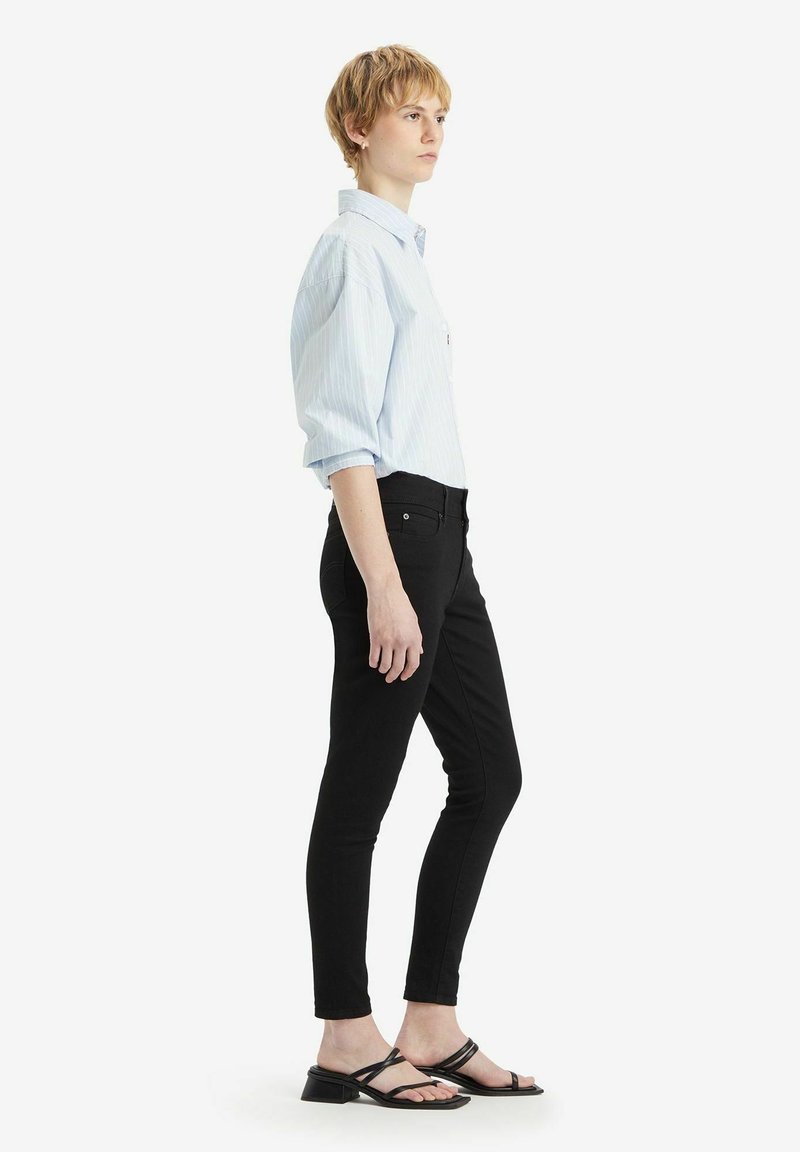 Chemise à rayures bleu clair à boutons, jean noir ajusté et sandales noires à lanières. Présente une coupe décontractée et des manches retroussées.
