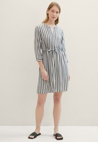 Robe rayée avec une patte de boutonnage et une taille à cordon. Couleurs gris et blanc, avec des manches trois-quarts et un ourlet au niveau des genoux.