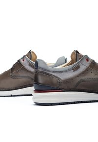 Zapatos de cuero marrón y tela gris con forma redondeada, diseño de cordones, acentos rojos en contraste y suela blanca gruesa.
