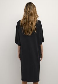 Abito nero oversize a maniche corte realizzato in materiale morbido, con una linea dritta che arriva poco sopra le ginocchia e un design minimale.