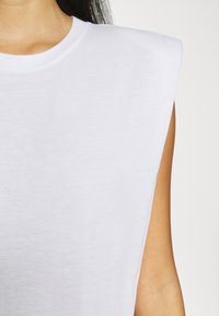 Biała bezrękawnik z wykrojem ramion o zdefiniowanej strukturze. Wykonana z miękkiej tkaniny, charakteryzująca się gładką teksturą i klasycznym okrągłym dekoltem.