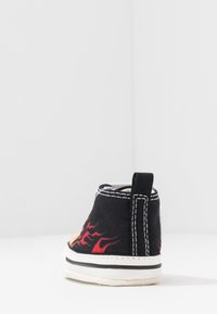 Czarna płócienna tenisówka z czerwonym wzorem płomieni, białym szyciem i czarną pętelką na pięcie. Niska cholewka z białą gumową podeszwą.