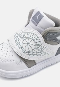 Baltos odinės sportinės bateliai su pilkais akcentais, perforuota nosis, ryškus SkyJordan logotipas su krepšinio kamuoliu ir sparnais, paminkštinta apykaklė patogumui.