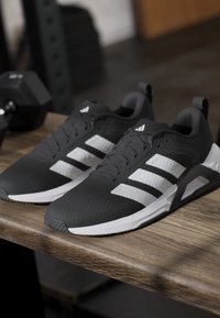 Black athletic shoes with white stripes, featuring a textured upper, cushioned sole, and black accents. Placed on a wooden surface.