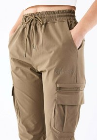 Pantalones cargo color caqui con cinturilla elástica y cordón. Incluyen bolsillos laterales y costuras decorativas con bordado de "Project x Paris".