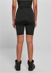 Shorts de sport noirs à taille haute, texture lisse et design ajusté, associés à des baskets montantes noires.