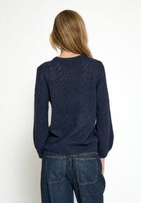 Marineblå strikket sweater med diamantmønster, rund hals og lange ærmer. Materialet virker blødt med en struktureret overflade.