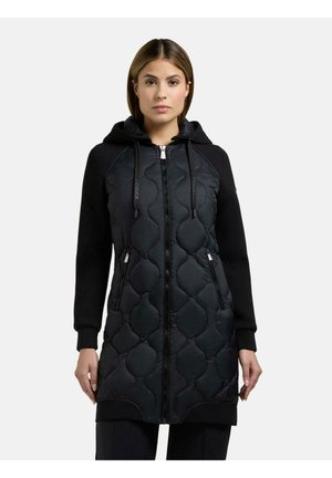 Frau trägt eine lange schwarze gesteppte Jacke mit Kapuze, Frontreißverschluss und Reißverschlusstaschen, steht vor einem schlichten hellen Hintergrund.