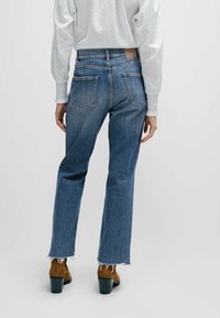 Högmidjade blå denimjeans med rakben, fransad fåll och bakfickor. Bärs med en texturerad vit topp och bruna klackboots.