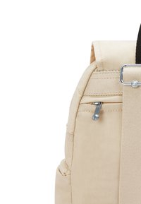 Zaino in tessuto beige con una superficie texturizzata, dotato di una tasca con zip e dettagli in metallo. Tasca laterale visibile per lo stoccaggio.