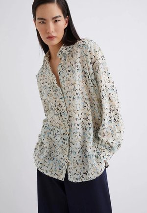 Camicia a maniche lunghe con bottoni di colore crema, decorata con un motivo geometrico in nero e blu. Realizzata in tessuto leggero e testurizzato, con una vestibilità comoda.