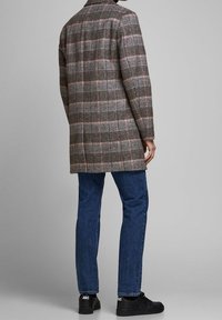 Cappotto a quadri grigio con maniche lunghe, colletto a scollo a V e taglio dritto; abbinato a jeans blu e sneakers nere. Tessuto testurizzato.