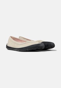 Ballerines en suède beige avec un bout arrondi, semelle en caoutchouc noire et motif de grip texturé. Détails de couture le long des coutures.