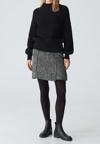 Zwarte gebreide trui met een hoge hals, gecombineerd met een grijze rok in een herringbone-patroon en zwarte enkellaarsjes. Glad textuur, aansluitend ontwerp.