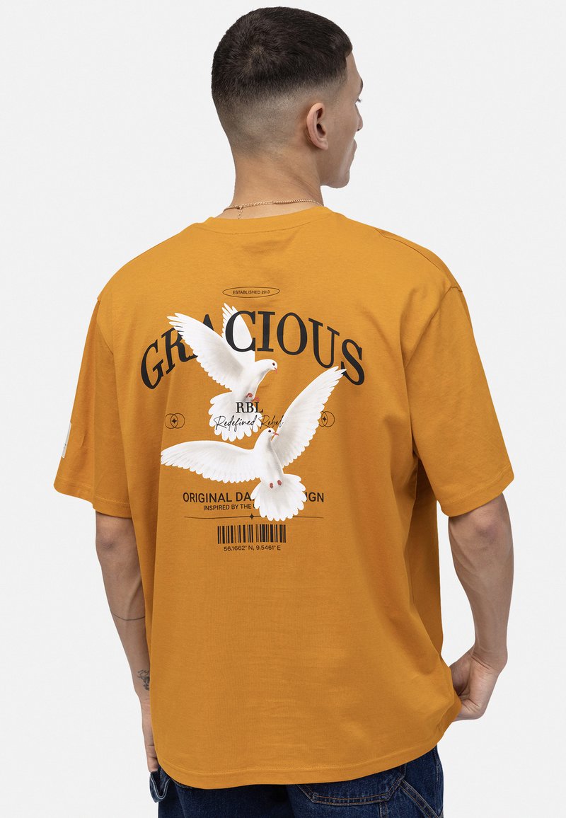 T-shirt en coton orange avec un design graphique de colombes blanches, le texte "GRACIOUS" et un code-barres au dos, col rond, manches courtes.