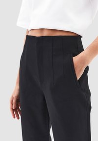 Zwarte op maat gemaakte broek met plooien, een gladde textuur en zijzakken, gecombineerd met een witte top met korte mouwen.