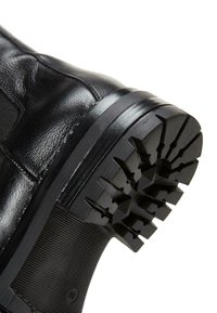 Black leather boot featuring a textured surface and a rugged, patterned rubber sole for enhanced grip and durability.