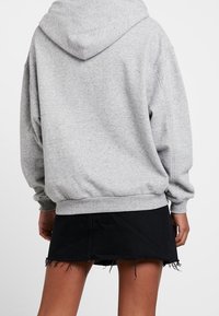 Sweatshirt à capuche gris avec une coupe ample, une texture douce et des poignets côtelés, associé à une jupe en denim noire avec un ourlet effiloché.