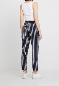 Navy och vita randiga byxor med avslappnad passform, elastisk midja och ankellängd, kombinerade med vita sneakers.