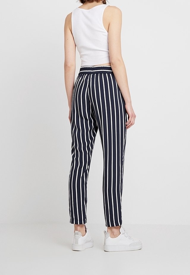 Navy och vita randiga byxor med avslappnad passform, elastisk midja och ankellängd, kombinerade med vita sneakers.