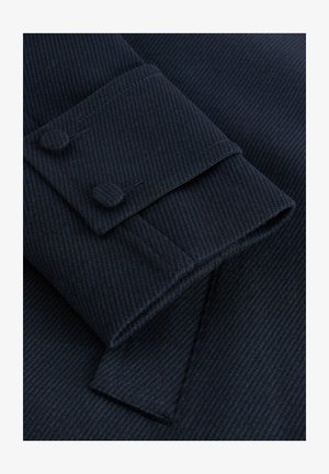 Navyblauwe gestructureerde stof met een fijn gestreept patroon. Bevat een manchet met twee knopen en een puntige flapdetail.