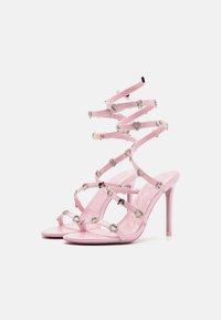 Pink high-heeled sandals with spiral straps adorned with heart-shaped accents and metallic embellishments. Smooth, glossy finish.