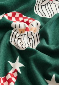 Zelená látka má opakující se vzor tváří Santy s červenými čepicemi, bílými plnovousy a černými pruhy na jemném povrchu.