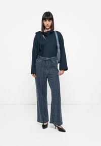Navy long-sleeve blouse with tie detail, paired with wide-leg blue textured trousers and black high-heeled shoes. Simple shoulder bag.