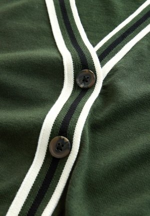 Grüne Strickjacke mit V-Ausschnitt, weißen und schwarzen Streifenakzenten sowie zwei dunklen Knöpfen. Weiche Textur mit gerippten Kanten.