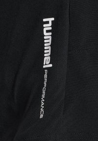 Czarna tkanina z białym pionowym napisem "hummel PERFORMANCE" nadrukowanym na niej.