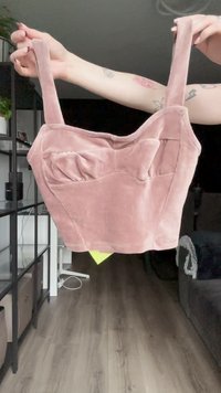 Vaaleanpunainen samettinen cropped-toppi leveillä olkaimilla, teksturoidulla pinnalla ja edessä solmulla. Muoto on tiukka, ja siinä on sileä, jämäkkä muotoilu.