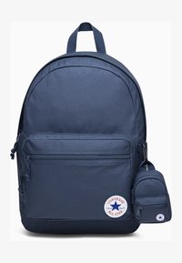 Sac à dos en tissu bleu marine avec une forme arrondie, poche zippée à l'avant, cordons de serrage sur les côtés et une petite pochette détachable. Il présente un logo circulaire.