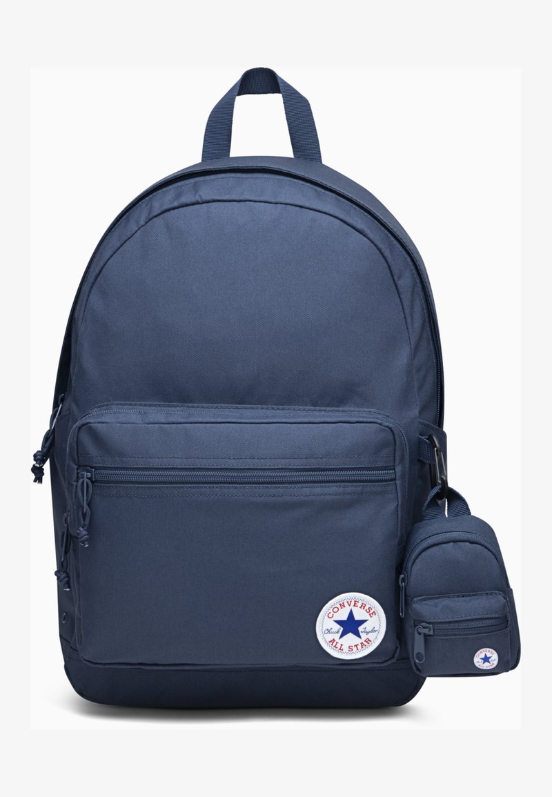Sac à dos en tissu bleu marine avec une forme arrondie, poche zippée à l'avant, cordons de serrage sur les côtés et une petite pochette détachable. Il présente un logo circulaire.