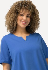 Modrý krátký rukáv top s výstřihem ve tvaru V. Vyrobeno z hladké tkaniny s volným střihem a minimálními švy.