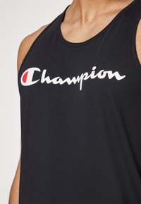 Top sin mangas de algodón negro con un prominente logo blanco de "Champion" con un acento rojo. La tela es suave y tiene un corte relajado.