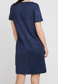 Granatowa sukienka z krótkim rękawem o gładkiej, miękkiej teksturze. Posiada okrągły dekolt oraz prosty krój, z detalem w postaci szwu z tyłu.