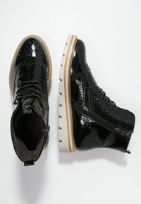 Botines de charol negro con detalles de brogue, cordones, cremallera lateral y una suela blanca gruesa. Textura suave y acabado brillante.